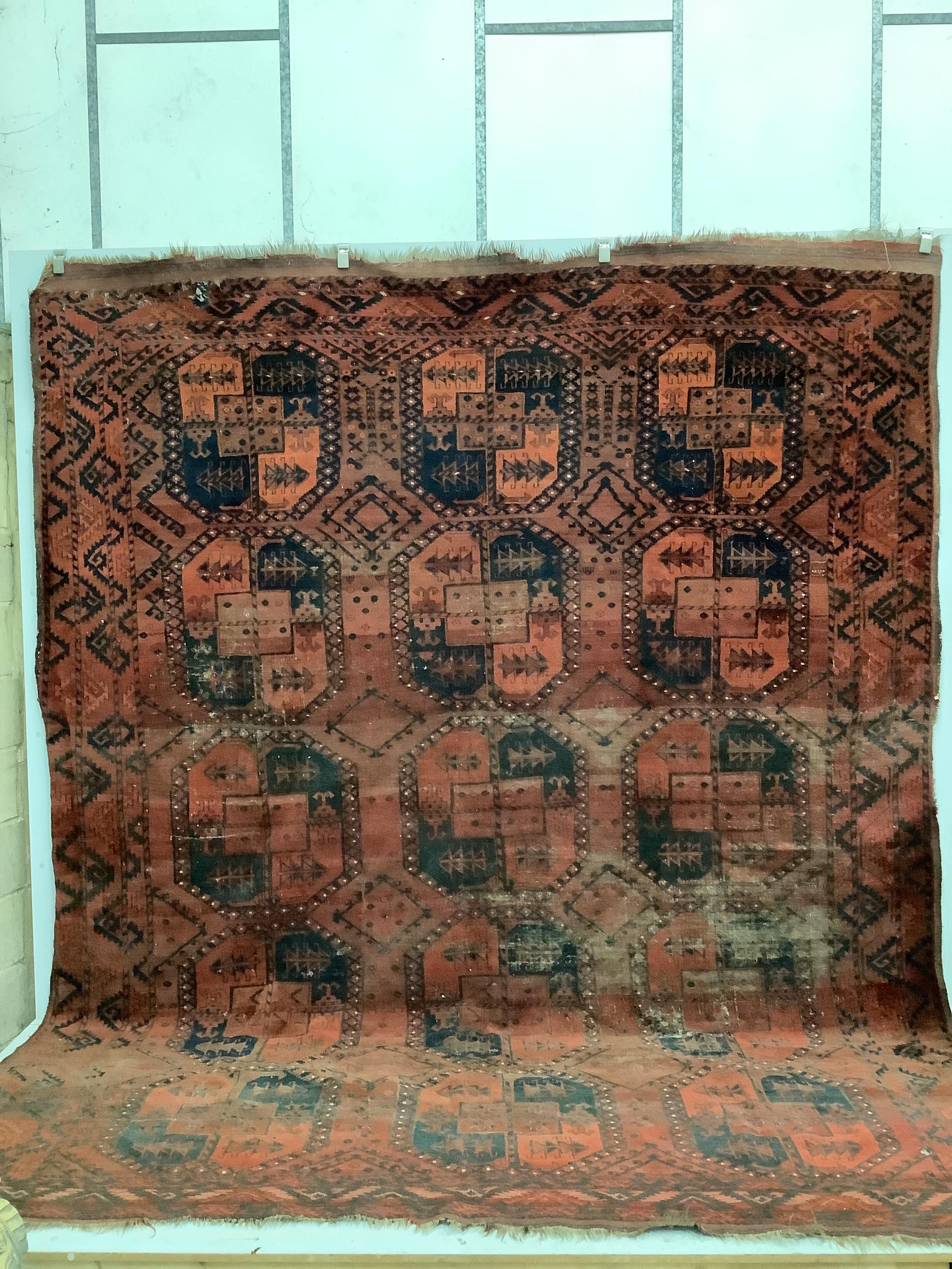 An antique Afghan red ground carpet, 340 x 278cm, worn and holed